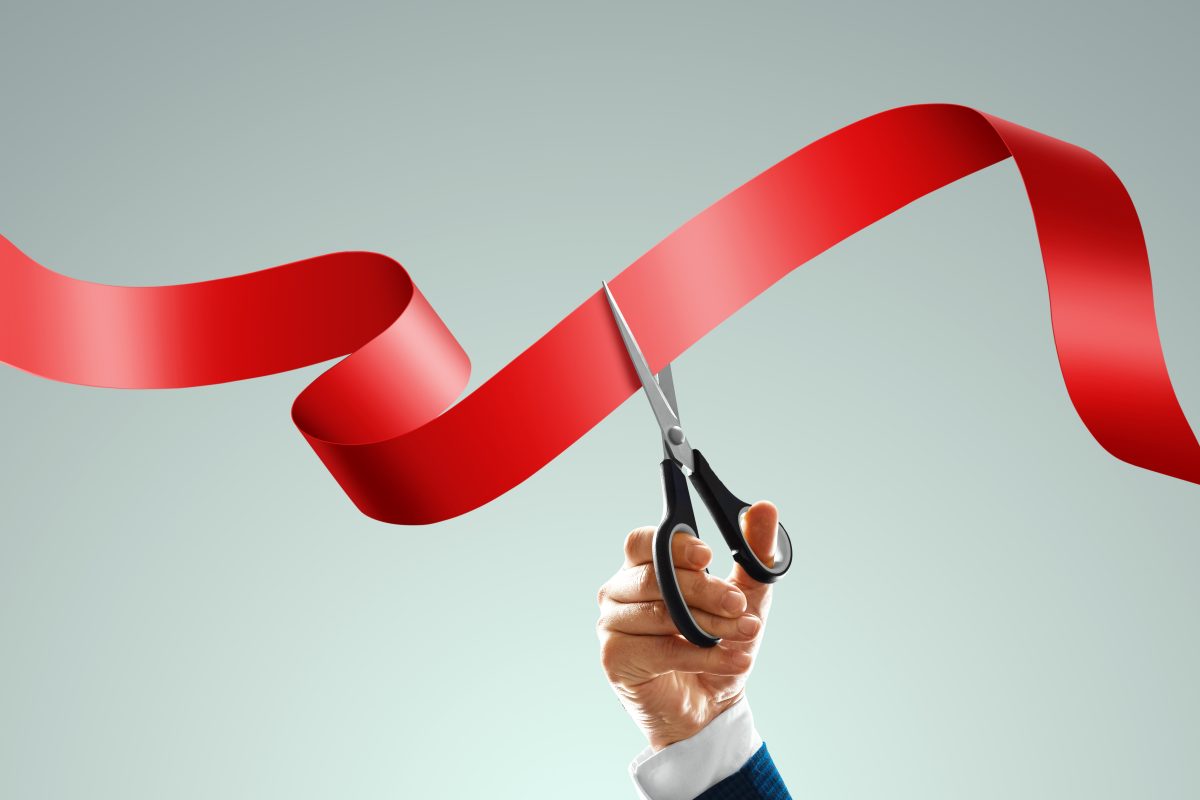 grand,opening,with,red,ribbon,and,scissors.,a,businessman's,hand