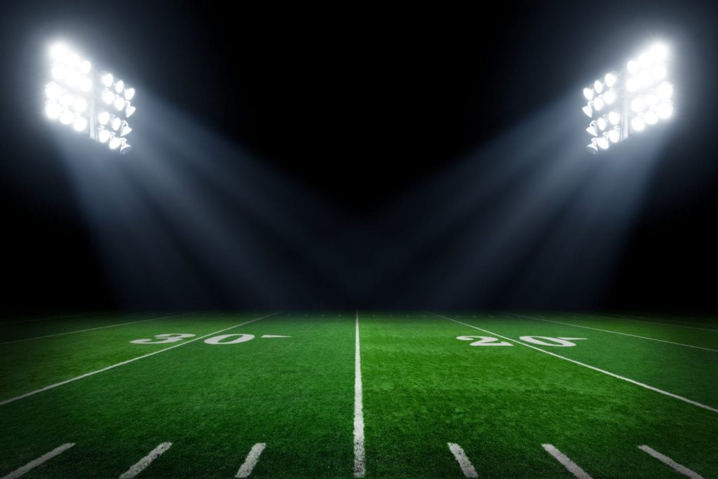 Football field at night with stadium lights.