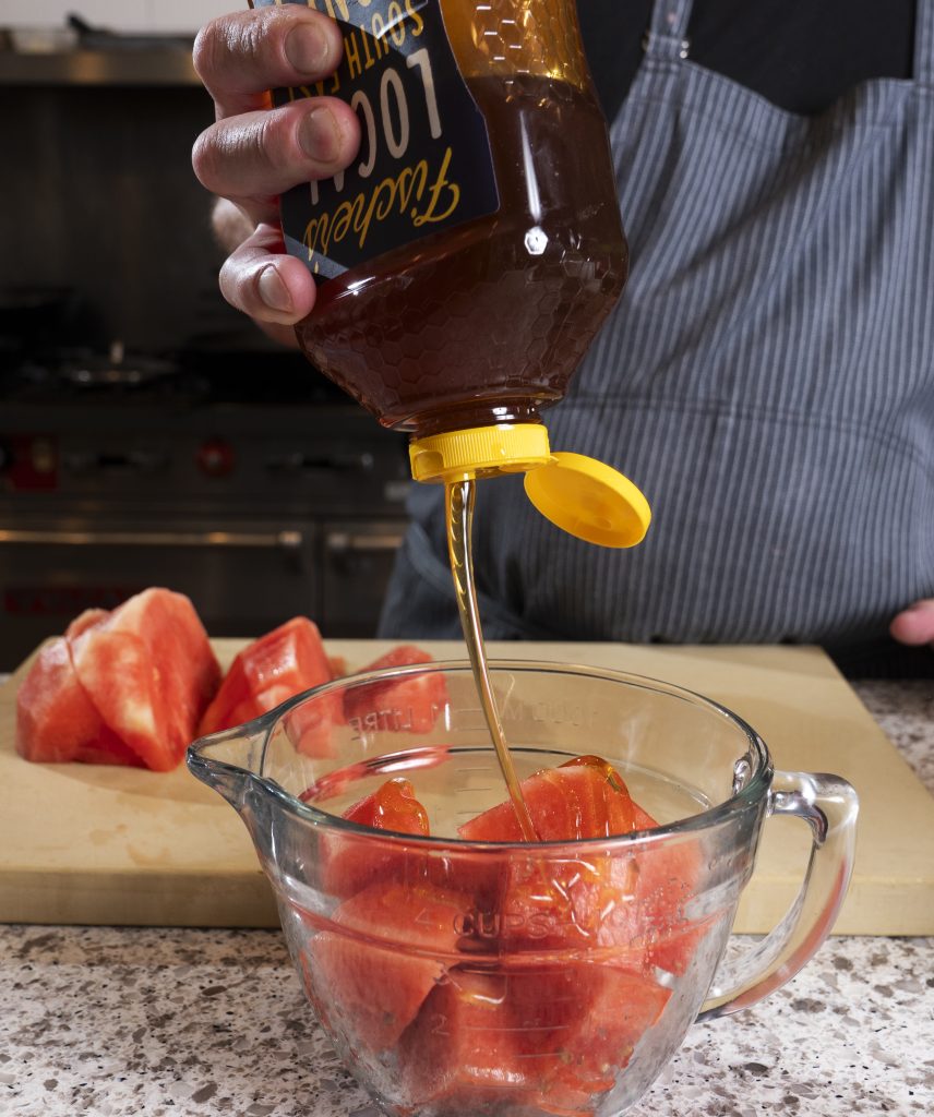 honey being poured on top of chopped watermelon in a bowl